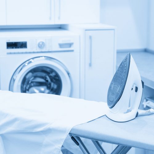 Iron on ironing board with white shirt in modern laundry room